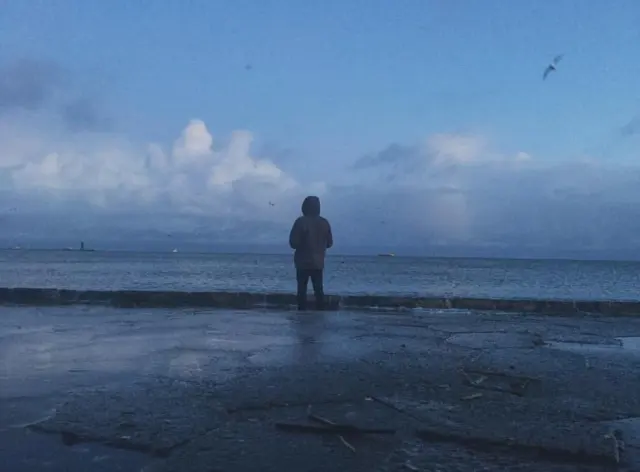 A person standing by the sea beneath clouds