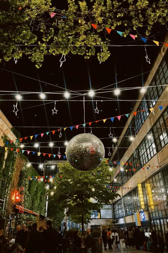 A mirror ball beneath string lights and leafy branches